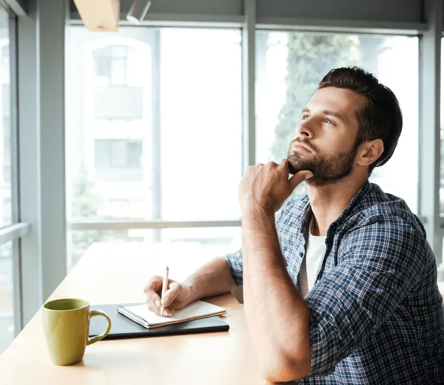 A man at a desk thinking, pen and notebook in hand