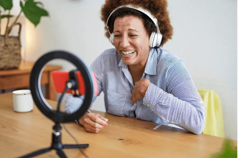 A woman wearing headphones recording to a smartphone on a ring light