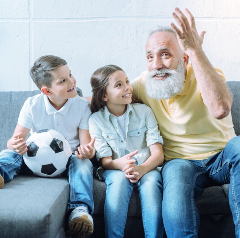 A grandfather on the sofa telling a story to his two grandchildren