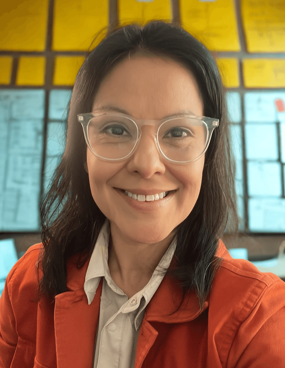 Adrianne, founder of Pivot Pronto Workshops, smiling in clear glasses and an orange jacket